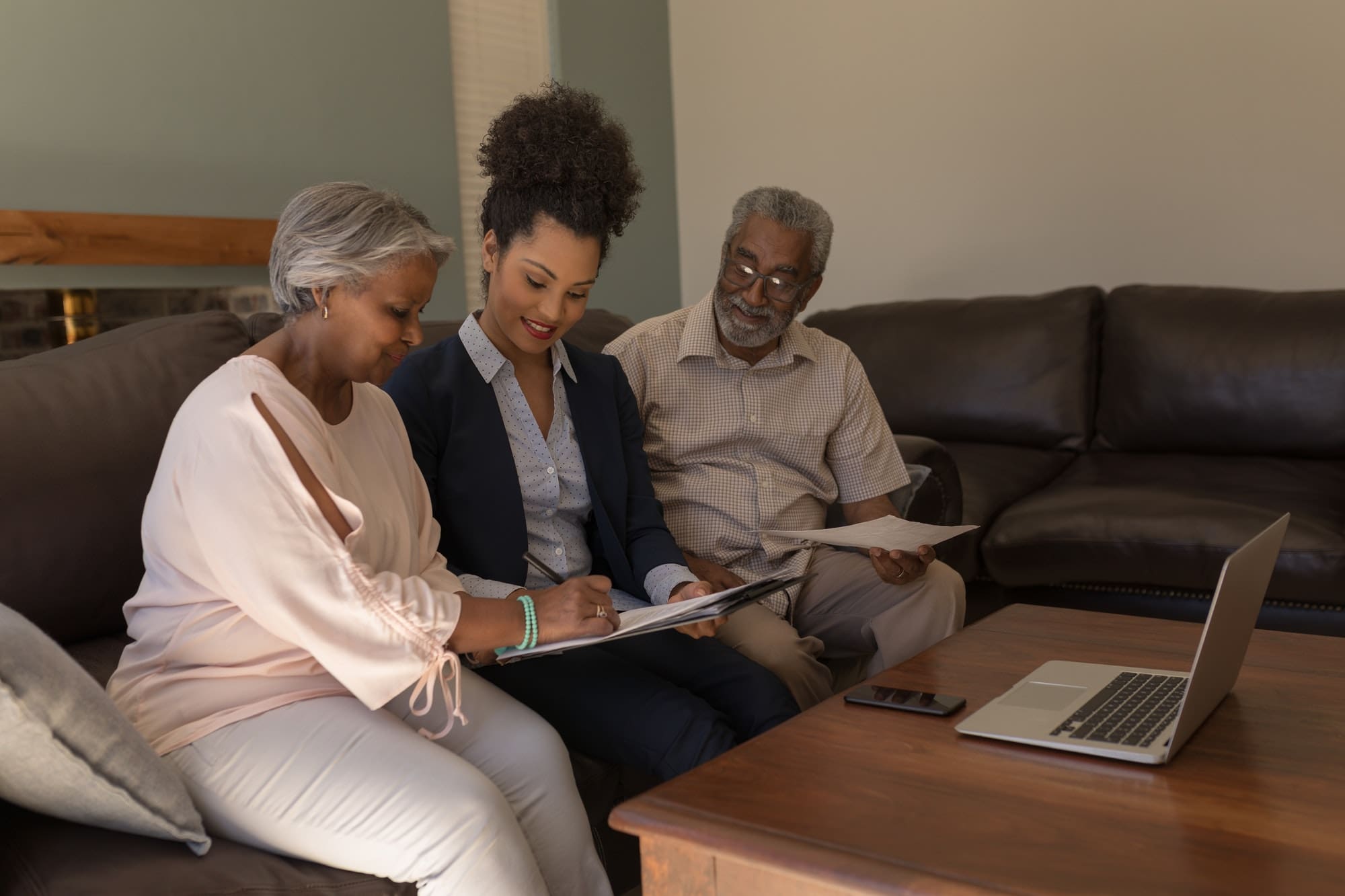 Woman signing property contract with real estate agent and senior man in living room at home